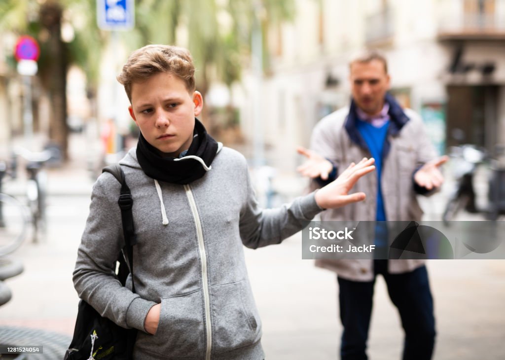 Frowning teenager gesturing enough while man reprimanding him Frowning teenager gesturing enough while adult man reprimanding him on city street Teenager Stock Photo