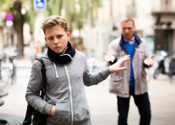 Frowning teenager gesturing enough while adult man reprimanding him on city street