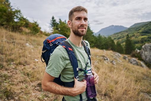 Handsome, aspired and confident young male hiker with a backpack hiking in nature.