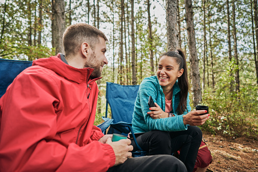 Alegre pareja de camping disfrutando de hablar y té en el bosque photo