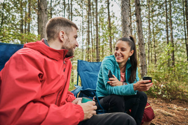 alegre pareja de camping disfrutando de hablar y té en el bosque - jpg fotografías e imágenes de stock