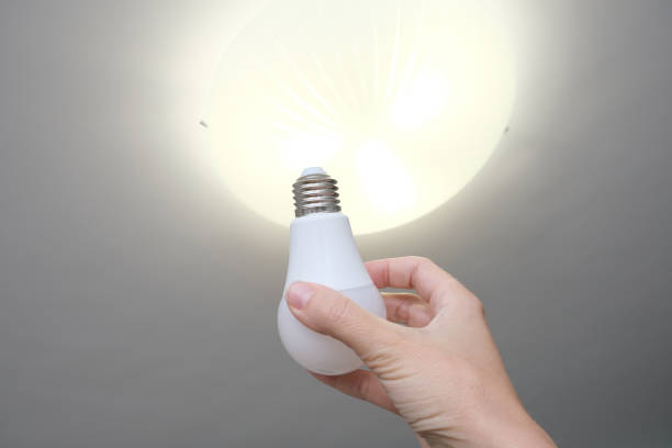 istock Female hand holding a led light bulb to change, replace it at home, screwing in the bulb into a lamp holder for energy saving and economy, saving money 1281528231