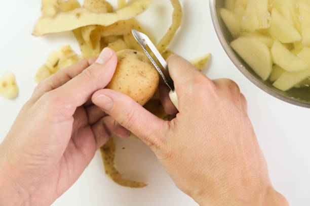 mains d’une femme au foyer épluchant la pomme de terre crue avec un couteau spécial d’outil près vers le haut, vue supérieure - root vegetable raw potato human skin root photos et images de collection