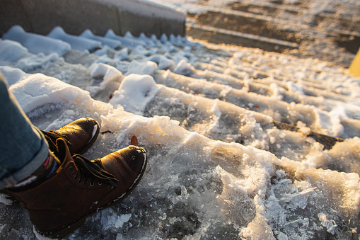 Peligro de resbalar. Botas femeninas sobre superficie de hielo de zapatillas ásperas. Una mujer con zapatos de cuero marrón desciende la escalera de hielo resbaladiza photo