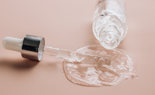 Bottle of hyaluronic acid on skin color background with oxygen bubbles. Selective focus