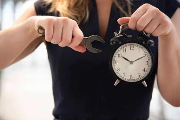 Photo of Business woman try to adjust time on alarm clock after shocked with late in rush hours when going to work in city urban background. Deadline and wake up late. People lifestyle daily life concept.