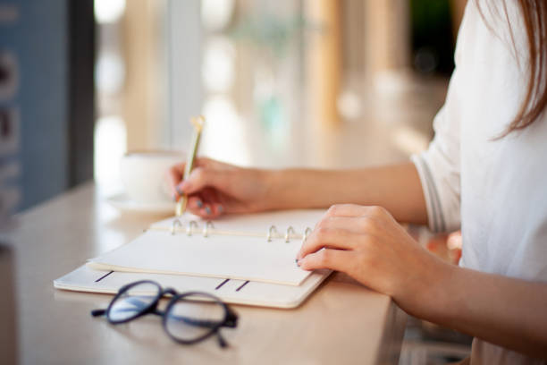 Young businesswoman in eyeglasses planning and writing down the daily schedule with in agenda Young businesswoman in eyeglasses planning and writing down the daily schedule in agenda. Time management and calendar reminder event for planner concept. Planning appointment and meetings. list stock pictures, royalty-free photos & images