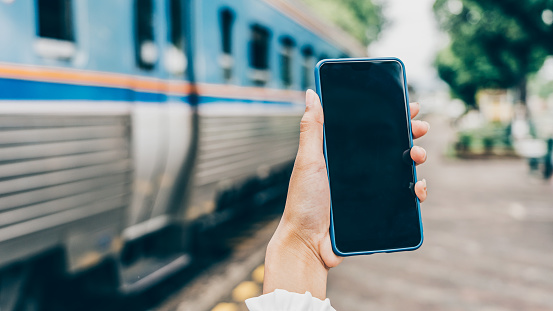 Young woman hands holding mobile at railway station for searching hotel room for booking and payment by internet cashless.