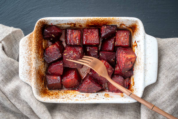 Baked red beetroot with honey, close up. Ceramic bowl with purple beet slices background, top view, macro