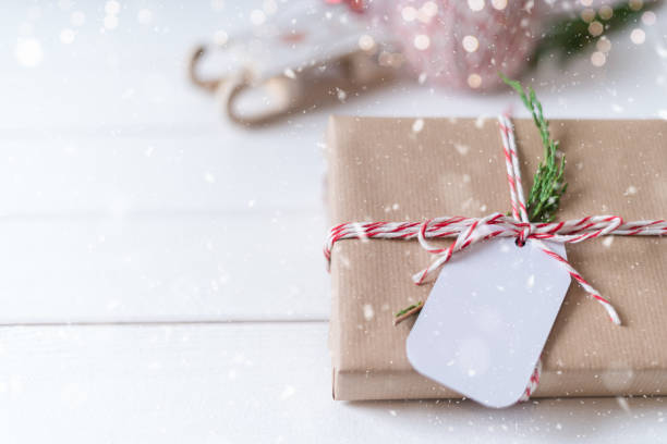 istock Christmas eco gift with empty tag. Glowing snow bokeh, coniferous branch. Winter holidays mock up on white background. Zero waste, plastic free. 1281577029