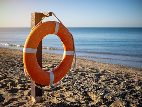 Bright orange lifebuoy on a sandy beach on a Sunny summer day. a lifebuoy with a rope and space for text or images.
