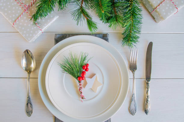 istock Christmas table setting with traditional Christmas decoration in white red tone. Beautiful festive dinner background. Xmas tableware, plate with linen napkin and vintage cutlery, green fir branch and red berries 1281579624