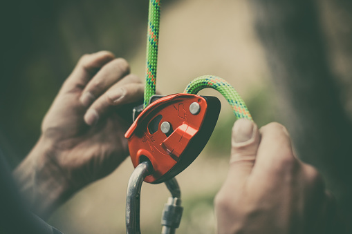 Close up shot of a man's hands operating a rock climbing belaying device.