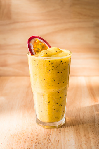 Passion Fruit shake with a slice of passion fruit on top for decor with a light wood background