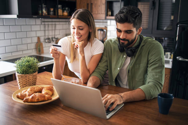 istock Happy couple using laptop at kitchen table with coffee and croissants 1281588292