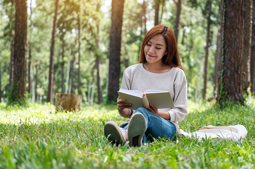 A beautiful young asian woman reading a book while sitting in the park