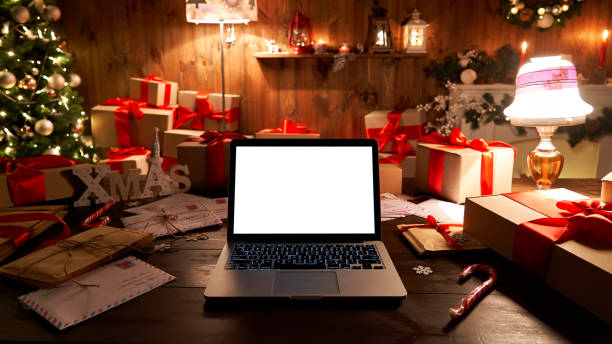 istock Laptop computer with white blank empty mock up screen on Merry Christmas table with presents gifts, decorated Xmas tree in Santa house background. Ecommerce website online shopping delivery ads. 1281596600