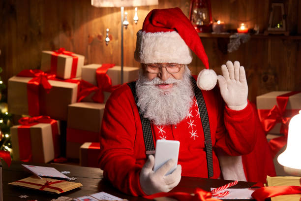 istock Happy Santa Claus holding smartphone video calling talking conferencing in virtual video online chat meeting sit at home table late with presents on xmas eve. Merry Christmas social distance concept. 1281596605