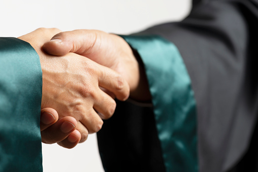 Two lawyers are shaking hands in front of white wall.