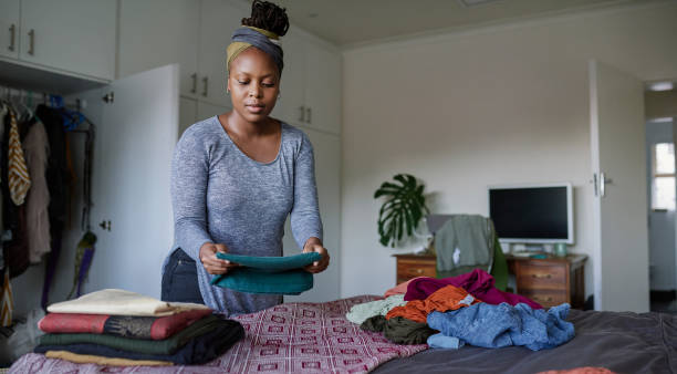 Cleaning day always end with packing away the washing Cropped shot of a young woman folding her laundry at home only women women bedroom bed stock pictures, royalty-free photos & images