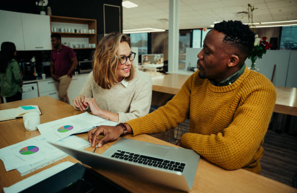 istock Young entrepreneurs working in office analysing pie charts and researching on laptop while colleagues chat over a cup of coffee 1281598572