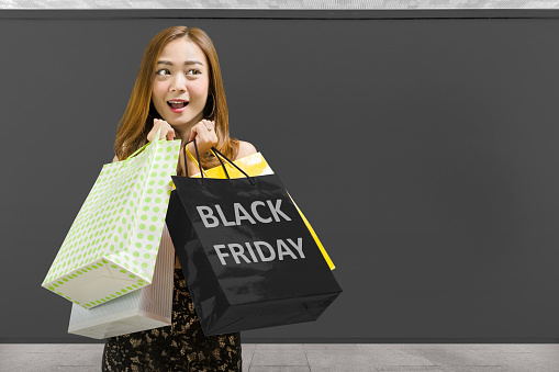 Asian woman carrying a shopping bag with a black wall background. Black Friday concept