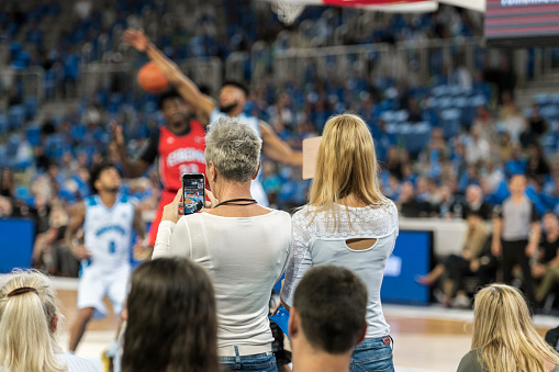 Rear view of two female spectators photographing with smartphone during the match.