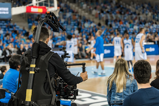 Rear view of cameraman shooting basketball match in stadium.