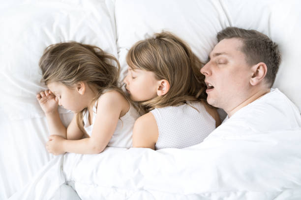 子供、娘、お父さんは毛布の下の枕の上でベッドで一緒に寝ます。父は一生懸命いびきをかいている。家族の共同睡眠。不眠症、夜の就寝時間。いい夢、見てね。アーリーウェイクアップ,幼 - uprise ストックフォトと画像