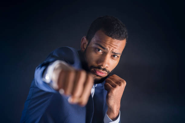 Close-up of businessman in punch stance Portrait of businessman in punch stance against black background at night. fighting stance stock pictures, royalty-free photos & images