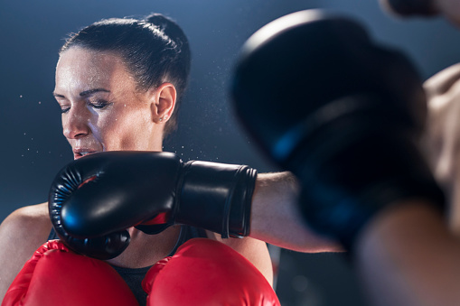 Female boxer getting punched in the face against black background.