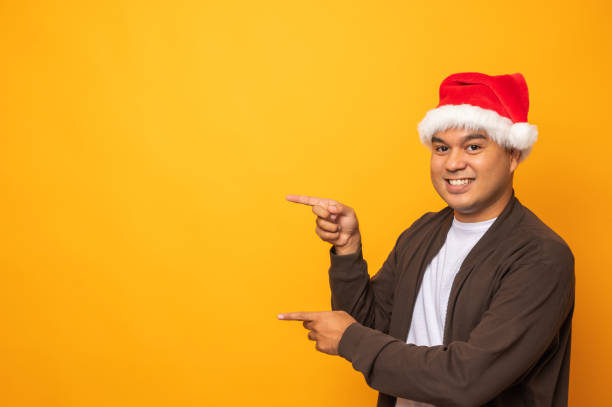 istock Young handsome asian man wearing christmas hat and pointing finger into blank space. Merry christmas and happy new years people theme concept. 1281608371