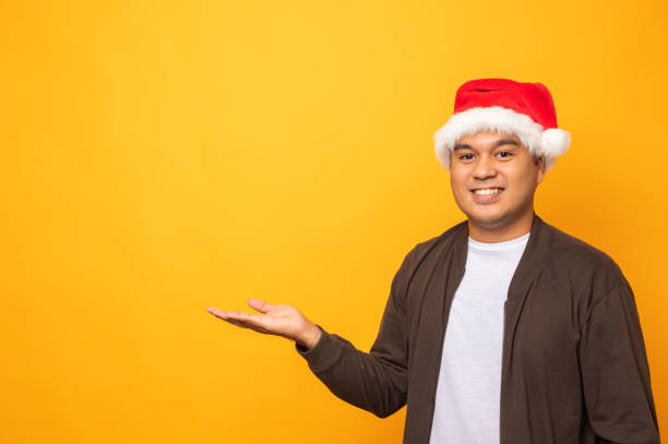 Young handsome asian man wearing christmas hat and open hand palm up into blank space for text. Merry christmas and happy new years people theme concept.