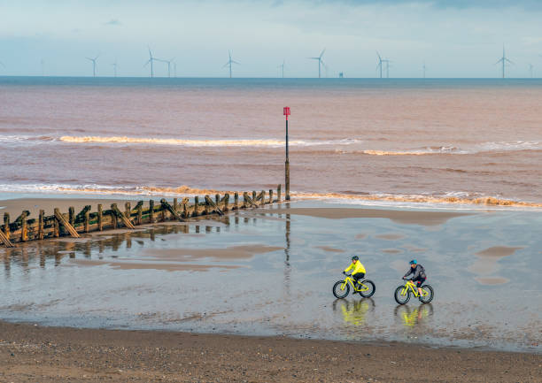 Cyclists on the beach Withernsea, East Yorkshire, England, 20/10/2020 - two colourful cyclists on a beach with groyne and wind farm in distance. east riding of yorkshire photos stock pictures, royalty-free photos & images