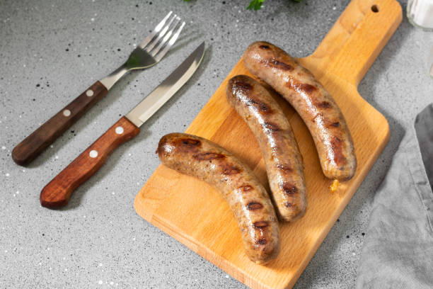 istock Grilled sausages on a wooden Board on a light gray kitchen table. View top 1281610936