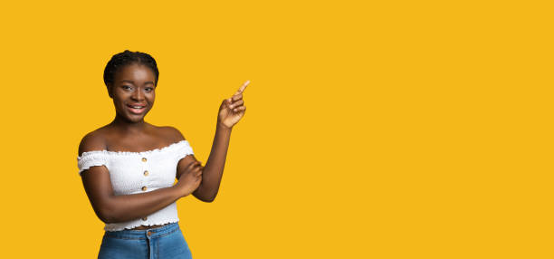 istock Smiling Young Black Lady Pointing Finger At Copy Space On Yellow Background 1281611275