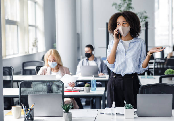 istock Talking with client in workspace and return after quarantine. Employees work in office with laptops and antiseptics, focus on african american woman 1281612120