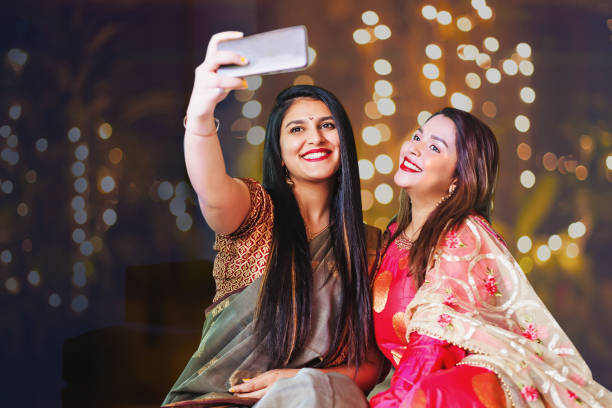 Diwali selfie Two beautiful Indian woman taking selfie while wearing ethnic traditional clothes for Diwali or another festival celebration sari stock pictures, royalty-free photos & images