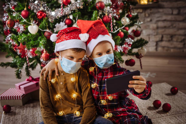 istock Two siblings with protective face masks on taking Selfie in front of the Christmas tree 1281613570