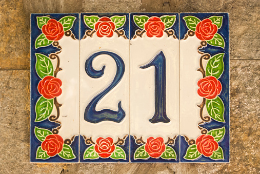 Weathered grunge square faience enameled decorated plate of number of street address with number 21 closeup
