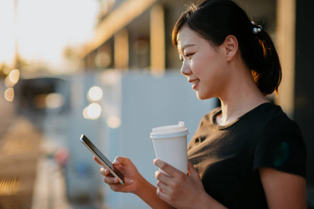 istock Young asian woman using smartphone and having take out coffee 1281618595