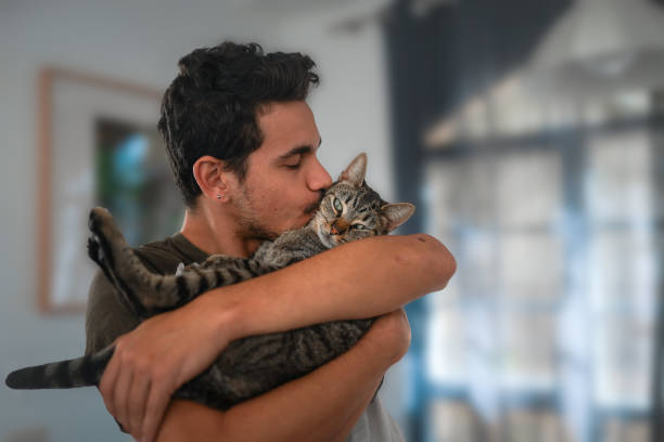 젊은 남자 보유 a 태비 고양이 에 그의 팔 ��과 키스 그것 - pets stroking licking love 뉴스 사진 이미지