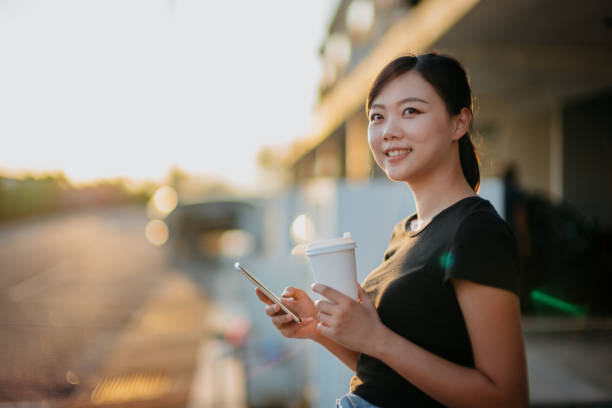 istock Young asian woman using smartphone and having take out coffee 1281621977