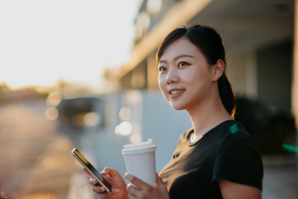 istock Young asian woman using smartphone and having take out coffee 1281621994