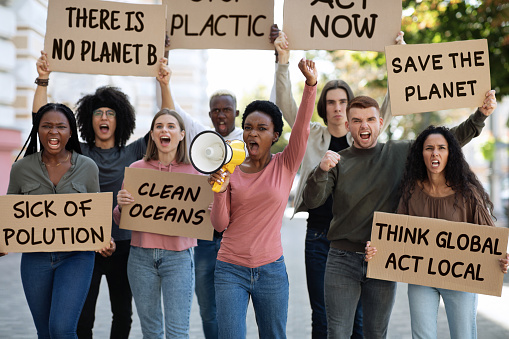 Motivated group of demonstrators striking on the street, fighting for environmental protection. Multiracial group of young people with placards protesting for healthy environment, green planet