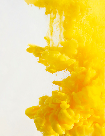 Yellow ink dropped into the water creating beautiful shapes and colored clouds. Abstract yellow background with copy space.