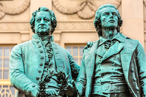 Weimar, Germany - December 23, 2014: The Statues of Goethe and Schiller Located in Weimar.\n\nThe statues of Johann Wolfgang von Goethe and Friedrich Schiller, located in Weimar, Germany, are iconic monuments paying tribute to two of the country's most renowned literary figures. Positioned in front of the German National Theatre in Theaterplatz, the statues symbolize the enduring friendship and intellectual collaboration between Goethe and Schiller, who were pivotal figures in German literature during the Classical and Weimar Classicism periods.\n\nThe statues were unveiled in 1857 and sculpted by Ernst Rietschel. The monument features Goethe and Schiller in animated conversation, embodying the spirit of intellectual exchange and artistic collaboration that defined their relationship. The site has become a symbol of Weimar's cultural heritage, attracting visitors and literature enthusiasts from around the world. It stands as a fitting tribute to the profound impact Goethe and Schiller had on German literature and intellectual thought during a pivotal era in the country's cultural history.