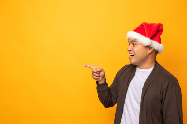 istock Young handsome asian man wearing christmas hat and pointing finger into blank space. Merry christmas and happy new years people theme concept. 1281627132