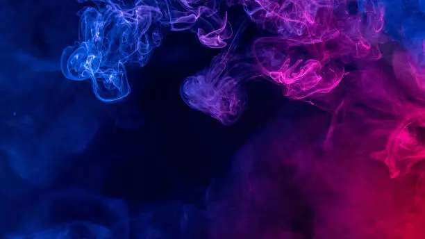 Photo of Conceptual image of colorful red and blue color smoke on dark black background.