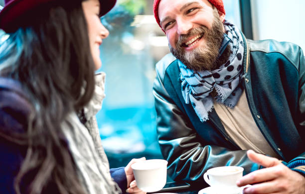 glückliches paar im gespräch und spaß zusammen in bar cafeteria - winter lifestyle konzept mit jungen menschen auf positive stimmung trinken italienischen kaffee - helle azurblaue filter mit fokus auf männlichegesicht - coffee couple italy drinking stock-fotos und bilder